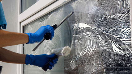 An employee of a professional cleaning service in overalls washes the glass of the windows of the...
