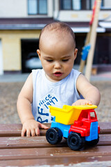 Cute happy smiling baby boy playing with colorful toy car at children playground outdoors