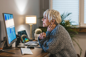 Focused old woman with white hair at home using PC computer. Senior stylish entrepreneur with...