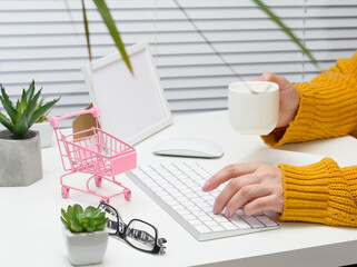 a woman in an orange sweater sits at a table and works at a computer. Remote work, freelance. Online shopping
