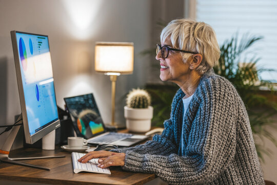 Elderly businesswoman working at her desk at the office reading through notes. Happy senior woman making online payments of bill using laptop. Smiling mature woman shopping online.