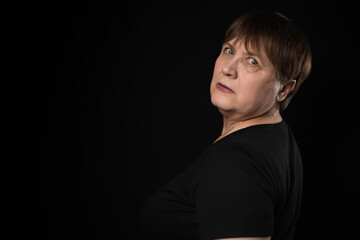 Grandmother with a serious look in a black T-shirt on a black background.
