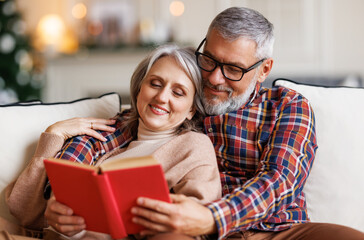 Young happy senior family couple in love enjoying Christmas holidays together at home, reading book