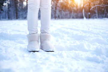 legs of a woman in fur boots on the snow in the forest. girl in warm shoes walks through the snowy forest. warm fur winter shoes