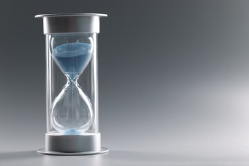Closeup of hourglass with blue sand on gray background