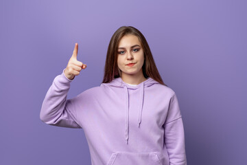 portrait of angry young woman pointing finger up, looking at camera with negative, standing over...