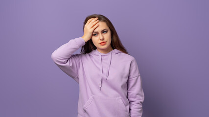 Young caucasian woman wearing a purple hoodie tired and very sleepy keeping hand on head, standing over purple background