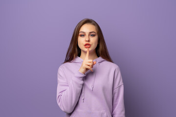 Portrait of beautiful young european woman with chestnut hair holding index finger at lips, asking to keep silence or not tell anyone her secret, saying Shhh, Hush, Tsss. Keep a secret