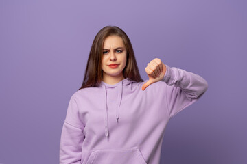 Dissatisfied young brunette woman showing her thumbs down in disapproval of offer situation while...