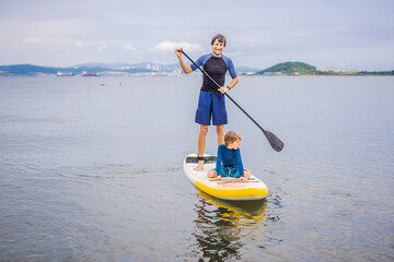 Father and son paddling on stand up board having fun during summer beach vacation
