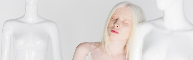 Albino woman with closed eyes standing near mannequin isolated on white, banner.