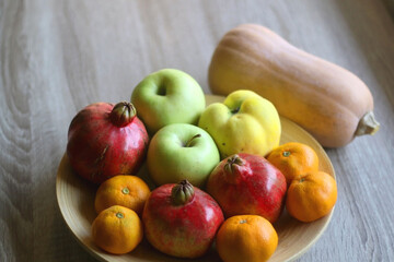 Wooden bowl filled with various seasonal fruit and butternut squash on a table. Selective focus.