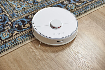 A white robot vacuum cleaner slides off the carpet. The robot vacuum cleaner changes the cleaning...