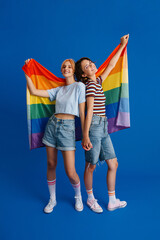 Excited lesbian couple holding hands while posing with rainbow flag
