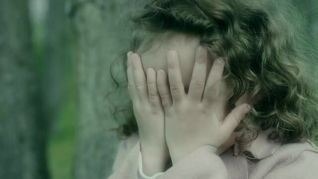 Little girl frightenedly covered her face with hands and cries.