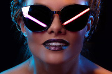 Neon style, reflection of neon lamps in dark glasses of a young stylish woman, close-up portrait on...