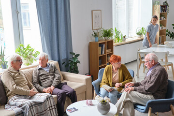 Elderly people sitting on sofa talking to each other and resting while spending time in nursing home