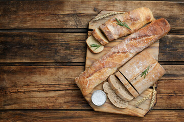 Cut fresh ciabatta and baguettes on wooden table, top view. Space for text