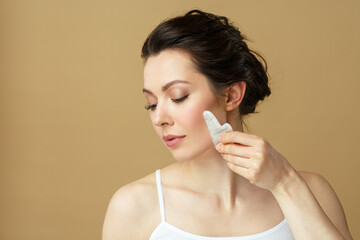 Portrait of a young woman using a facial massager made of natural rose quartz