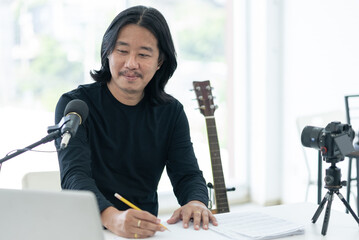 Asian artist man reading note with microphone and computer in home