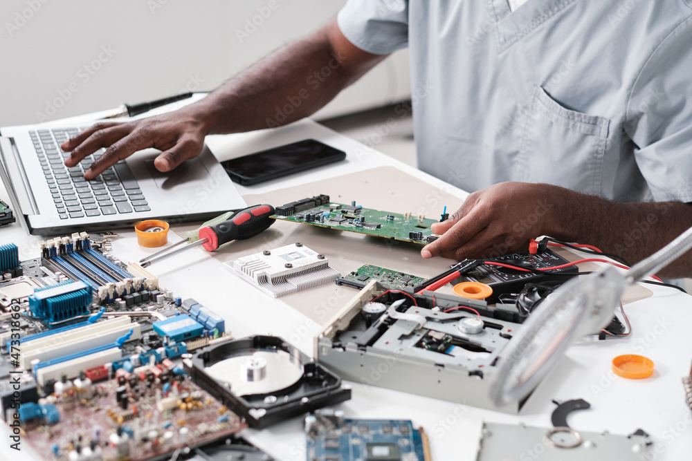 Poster hands of young blackman typing while holding part of hardware during repairing work