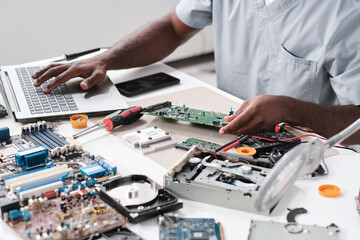 Hands of young blackman typing while holding part of hardware during repairing work