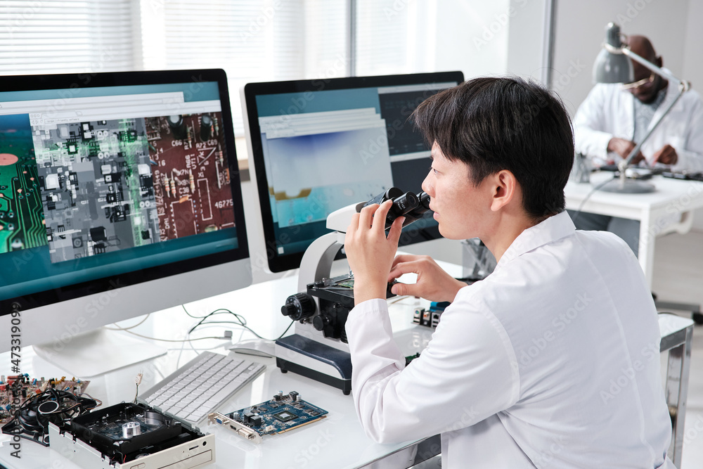 Poster young contemporary researcher with microscope looking at computer screen during work in scientific l
