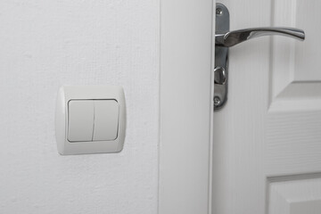 Modern light switch on white wall near door