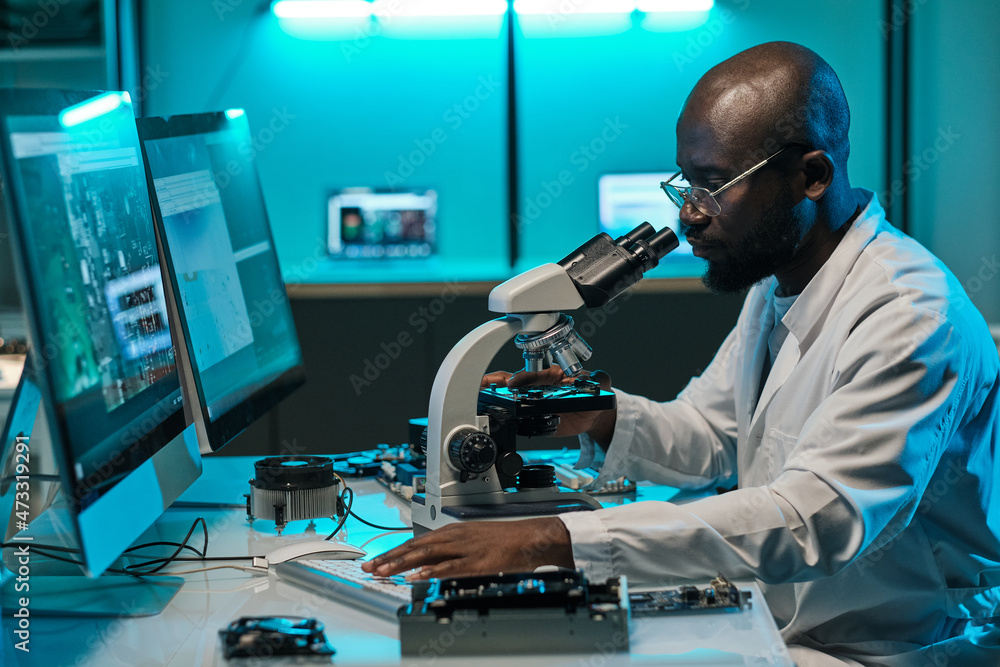Aufkleber young african researcher with microscope pressing key of computer keypad during work