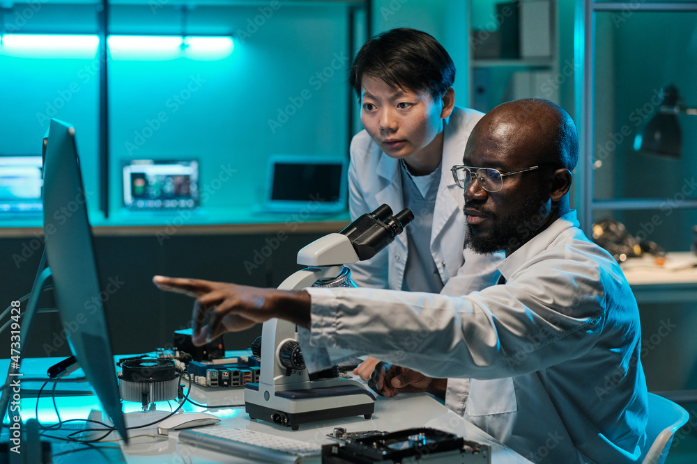 Poster Confident African scientist pointing at computer screen while explaining something to female colleague