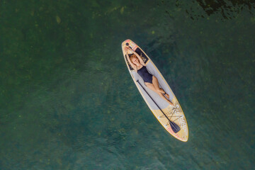 A woman lies on a sup, view from a drone. Young women Having Fun Stand Up Paddling in the sea. SUP....