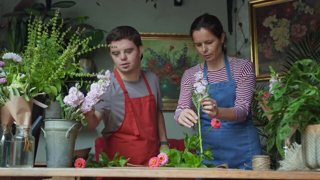 Young male florist with Down syndrome working with help of mentoring colleague indoors in flower shop