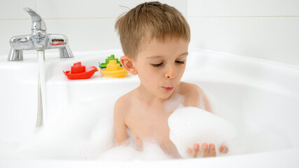 Happy smiling boy having bath and playing with soap foam. Concept of hygine, children development and fun at home
