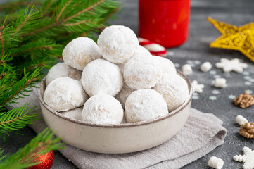 Fototapeta na wymiar Christmas snowball cookies with walnuts and powdered sugar in a bowl on a gray concrete background with a cup of cocoa. Copy space.