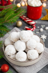 Fototapeta na wymiar Christmas snowball cookies with walnuts and powdered sugar in a bowl on a gray concrete background with a cup of cocoa. Copy space.
