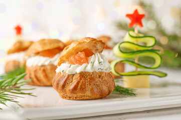 Obraz na płótnie Canvas Festive savory profiteroles with salmon, cream cheese and dill on a white plate on a white background. Appetizer for Christmas and New Year. Selective focus.