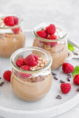 Chocolate mousse with whipped cream and fresh raspberries in a glass on a gray concrete background. Copy space.