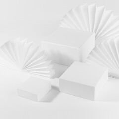 White abstract stage mockup with three different size square podiums for presentation cosmetic product, goods on table with simple geometric decor - asian paper fans, top view, corner, 3d, square.