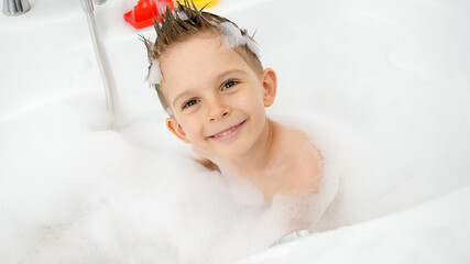 Portrait of happy smiling boy washing in bath with soap suds and looking in camera. Concept of...