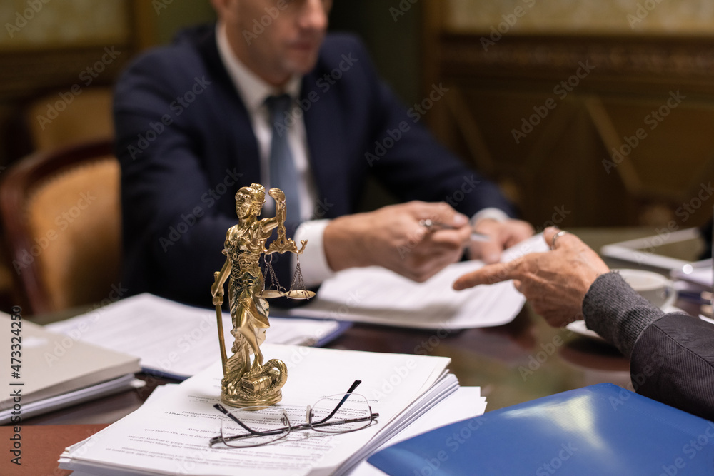 Aufkleber statue of justice and eyeglasses on stack of juridical papers on table where two lawyers discussing 