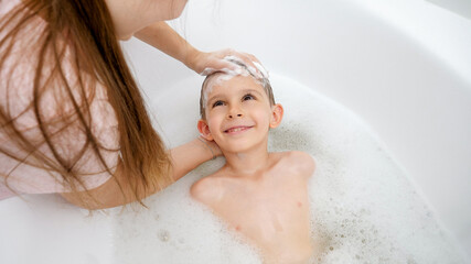 Little smiling boy with mother washing head in bath