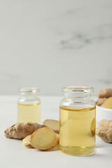 Glass bottle of essential oil and ginger root on white table