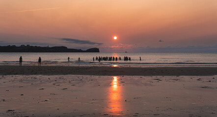 Sun setting over silhouettes of people relaxing on coastal beach