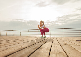 Fit woman in sportswear practicing deep squats on the beach early morning