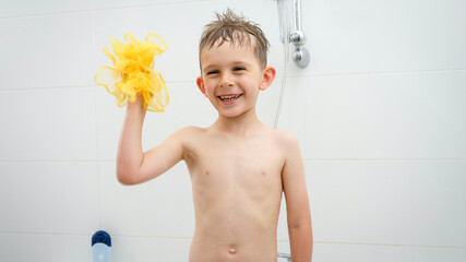 Happy laughing boy playing with yellow sponge while washing under shower in bath. Concept of hygine, children development and fun at home