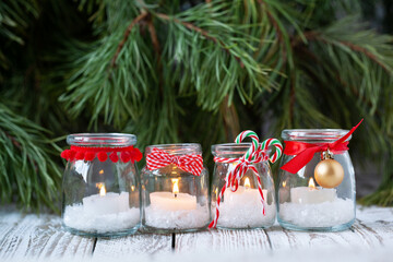 Four candles in glass jars with fir on holiday background. Cozy handmade holiday home decor: glass...