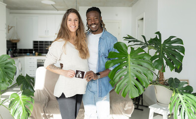 Smiling man with pregnant woman showing ultrasound scan in living room at home