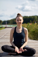 Fototapeta na wymiar Young relaxing smiling woman practicing yoga on the wooden pier near lake.