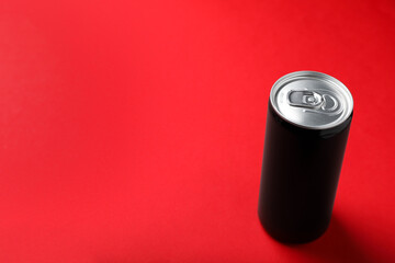 Black can of energy drink on red background. Space for text