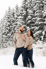 Walk in winter. Embracing couple enjoying snowfall. Man and woman having fun in the frosty forest. Romantic date in winter time.Christmas mood of a young family. Love and leisure concept